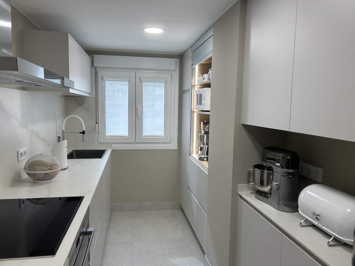 Minimalista cocina moderna con azulejos blancos y electrodomésticos integrados en reformas e interiorismo Eiroa.