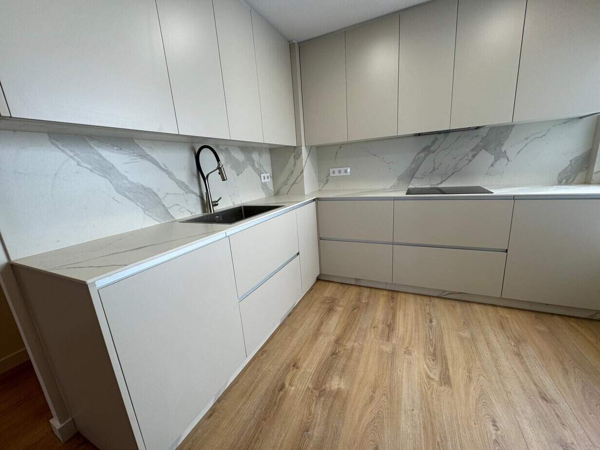Moderno diseño de cocina con mobiliario minimalista en tonos claros y granito en la encimera.